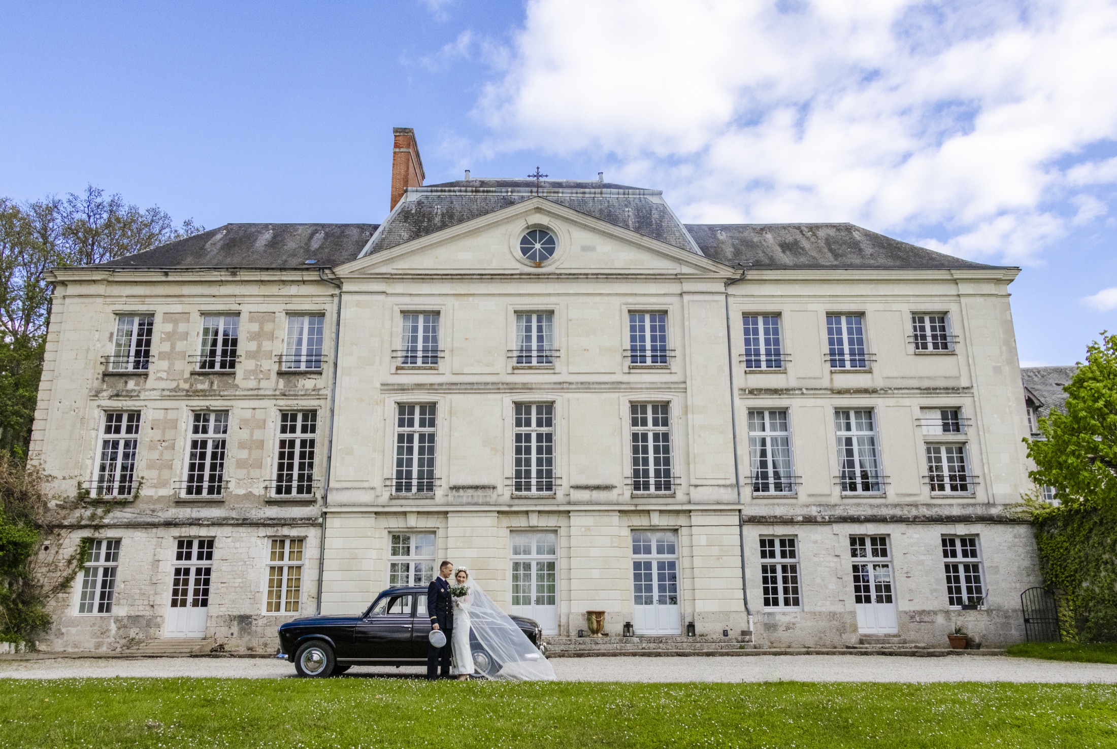 Les mariés devant la façade du château et la voiture ancienne